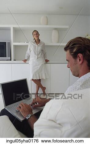 Young man working on a laptop with a young woman standing in front of him View Large Photo Image Stock Photograph - Young man working on a laptop with a young woman standing in front of him. Fotosearch