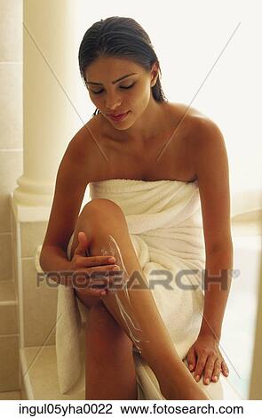 Stock Image - Young woman applying lotion on her legs. Fotosearch