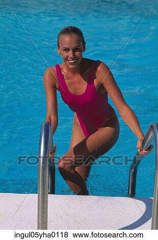 Stock Photo - Young woman climbing a swimming pool ladder. Fotosearch