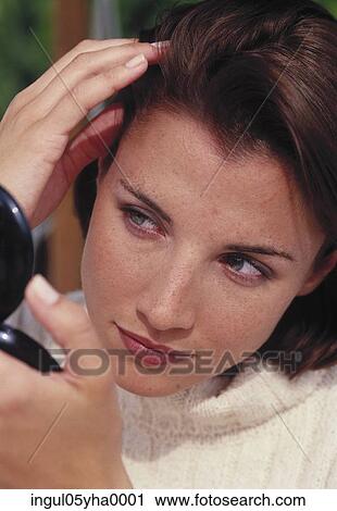 Stock Image - Young woman looking into a vanity mirror. Fotosearch