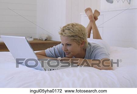 Young woman lying on a bed in front of a laptop View Large Photo Image Stock Image - Young woman lying on a bed in front of a laptop. Fotosearch