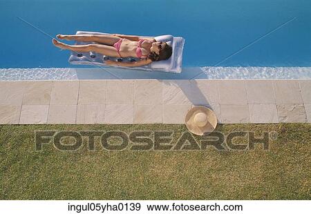 Stock Photo - Young woman lying on a pool raft in a swimming pool. Fotosearch