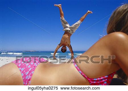 Young woman lying on the beach with a young man doing a handstand behind her View Large Photo Image Stock Photography - Young woman lying on the beach with a young man doing a handstand behind her. Fotosearch