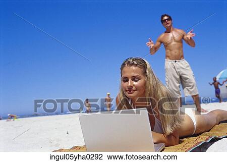 Young woman lying on the beach working on a laptop View Large Photo Image Stock Image - Young woman lying on the beach working on a laptop. Fotosearch