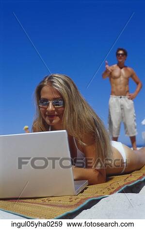 Young woman lying on the beach working on a laptop View Large Photo Image Stock Photo - Young woman lying on the beach working on a laptop. Fotosearch