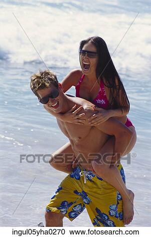 Stock Image - Young woman riding piggy back on a young man. Fotosearch