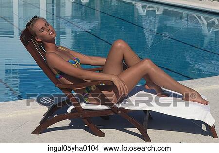 Young woman sitting on a lounge chair beside a swimming pool View Large Photo Image Picture - Young woman sitting on a lounge chair beside a swimming pool. Fotosearch