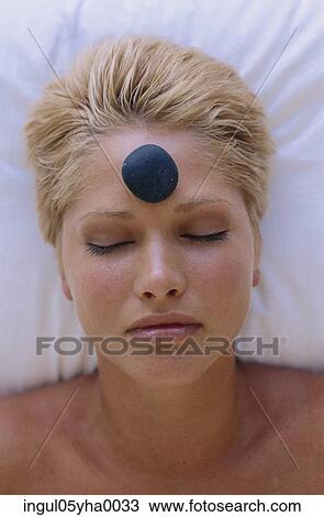 Stock Image - Young woman with a therapeutic stone on her forehead. Fotosearch