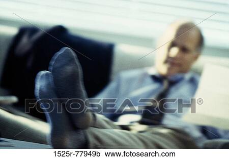 Stock Image - Businessman with his feet up on a desk holding a sheet of paper. Fotosearch