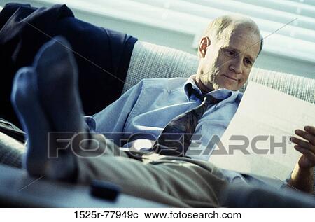 Stock Image - Businessman with his feet up on a desk holding a sheet of paper. Fotosearch