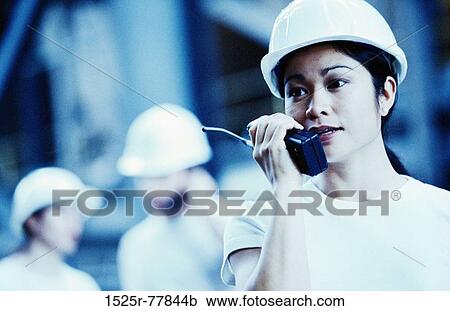 Stock Image - Female construction worker talking on a walkie-talkie. Fotosearch