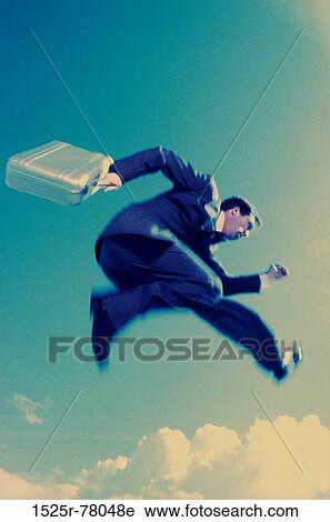 Stock Image - Low angle view of a businessman holding a briefcase in mid-air. Fotosearch