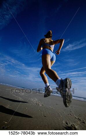 Rear view of a young woman jogging on the beach View Large Photo Image Stock Image - Rear view of a young woman jogging on the beach. Fotosearch