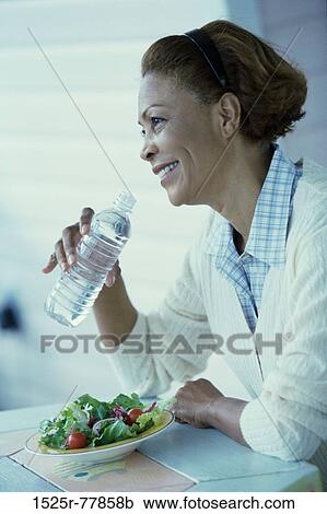 Stock Image - Side profile of a mid adult woman drinking water from a water bottle. Fotosearch