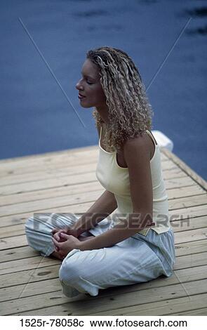 Stock Image - Side profile of a young woman meditating on a dock. Fotosearch