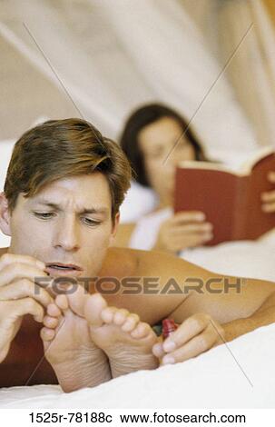 Stock Image - Young man applying nail polish on a young woman's toenails. Fotosearch