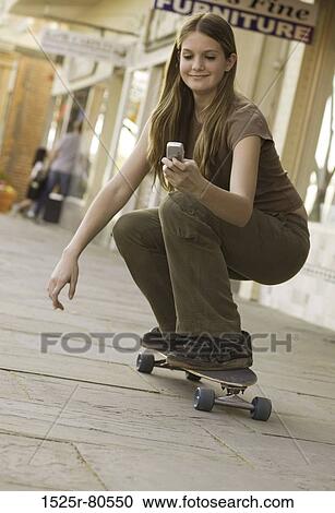 Close-up of a young woman on a skateboard and looking at a mobile phone View Large Photo Image Stock Image - Close-up of a young woman on a skateboard and looking at a mobile phone. Fotosearch