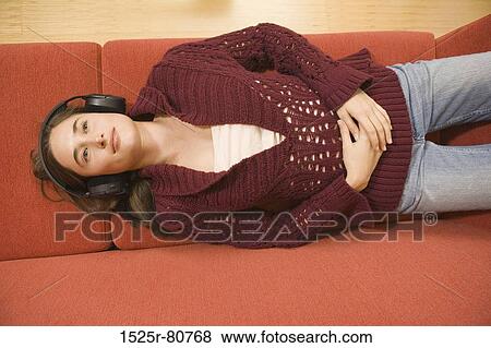 High angle view of a young woman lying on a couch and listening to music View Large Photo Image Stock Photo - High angle view of a young woman lying on a couch and listening to music. Fotosearch