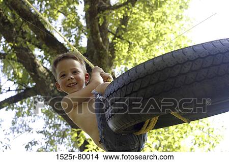 Low angle view of a boy swinging on a tire swing View Large Photo Image Picture - Low angle view of a boy swinging on a tire swing. Fotosearch