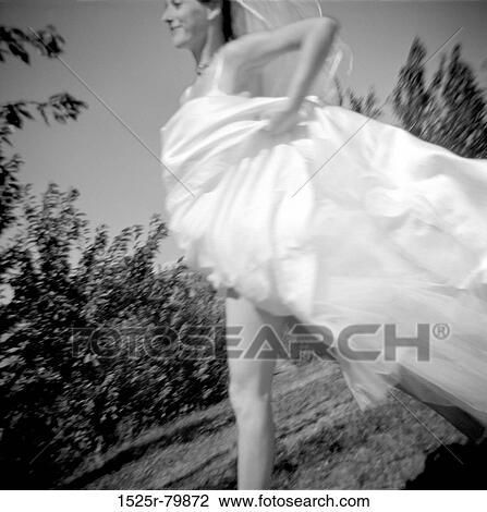 Stock Image - Low angle view of a bride running in a garden. Fotosearch