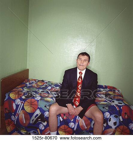 Mid adult man sitting on a bed View Large Photo Image Stock Image - Mid adult man sitting on a bed. Fotosearch