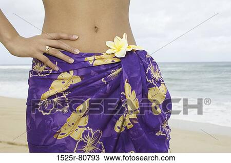 Stock Image - Mid section view of a woman standing on the beach with her hand on her hip. Fotosearch