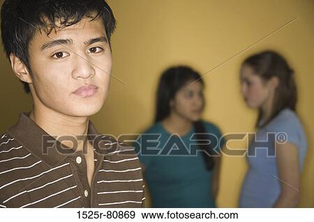 Stock Photo - Portrait of a teenage boy with two teenage girls talking in the background. Fotosearch