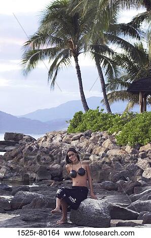 Portrait of a young woman sitting on a rock on the beach View Large Photo Image Picture - Portrait of a young woman sitting on a rock on the beach. Fotosearch
