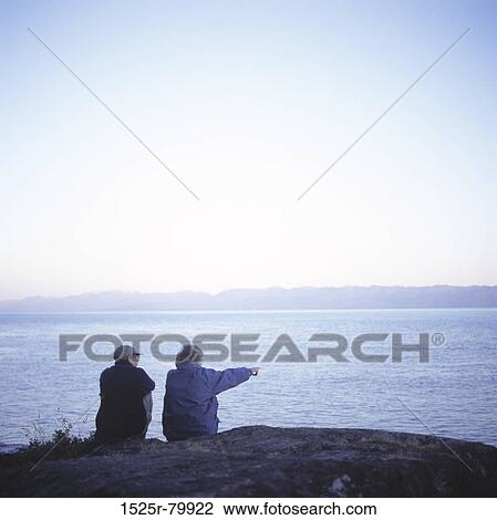 Rear view of a senior couple sitting together on a rock View Large Photo Image Stock Image - Rear view of a senior couple sitting together on a rock. Fotosearch