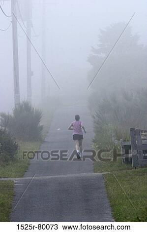 Stock Image - Rear view of a woman jogging on a road. Fotosearch