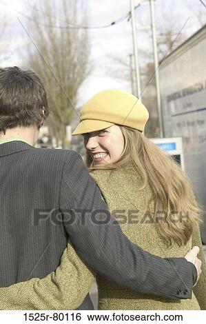 Stock Photograph - Rear view of a young couple walking with their arms around each other. Fotosearch