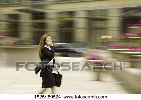 Side profile of a businesswoman talking on the mobile phone while walking View Large Photo Image Picture - Side profile of a businesswoman talking on the mobile phone while walking. Fotosearch