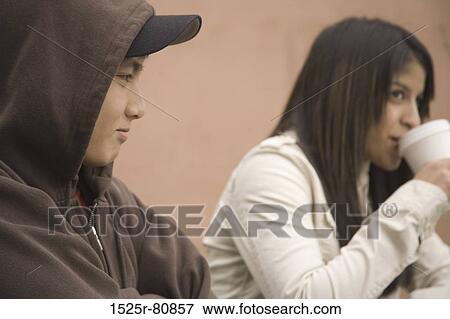 Stock Photo - Side profile of a young man with a young woman sitting beside him and drinking from a cup. Fotosearch