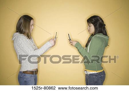 Side profile of two young women holding mobile phones View Large Photo Image Stock Image - Side profile of two young women holding mobile phones. Fotosearch