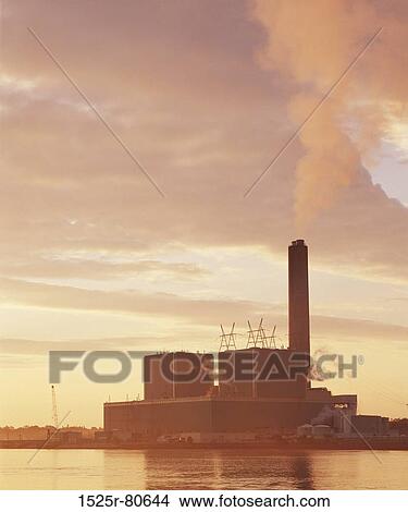 Smoke emitting from the chimney of a factory at the waterfront View Large Photo Image Picture - Smoke emitting from the chimney of a factory at the waterfront. Fotosearch