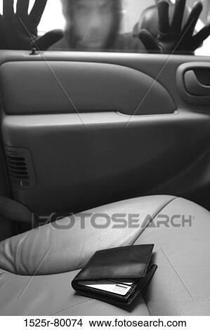 Picture - Thief looking at a wallet kept inside a car. Fotosearch