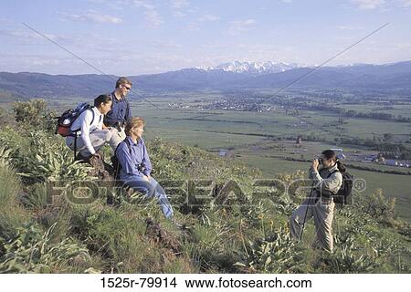 Young woman taking a photograph of a mid adult woman and two young men View Large Photo Image Picture - Young woman taking a photograph of a mid adult woman and two young men. Fotosearch