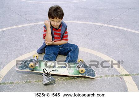 Boy sitting on the ground with a skateboard and holding his elbow View Large Photo Image Stock Photography - Boy sitting on the ground with a skateboard and holding his elbow. Fotosearch