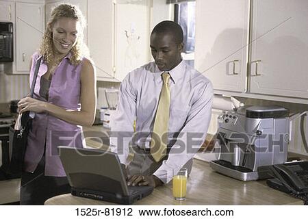 Stock Image - Businessman operating a laptop with a businesswoman standing beside him. Fotosearch