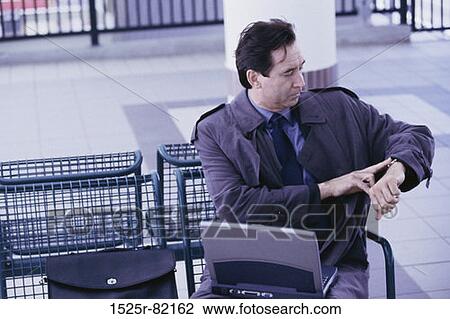 Businessman with a laptop sitting and looking at his wristwatch View Large Photo Image Stock Image - Businessman with a laptop sitting and looking at his wristwatch. Fotosearch