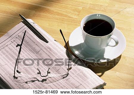 Stock Photo - Close-up of a cup of coffee near a newspaper pen and eyeglasses. Fotosearch