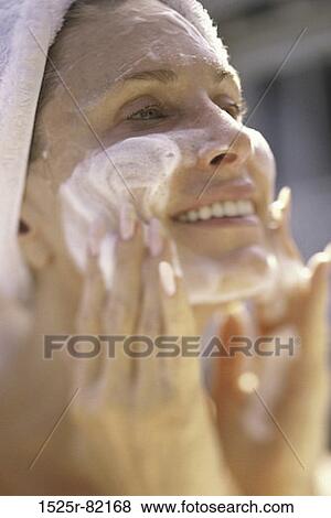 Stock Photo - Close-up of a young woman applying lotion to her face. Fotosearch