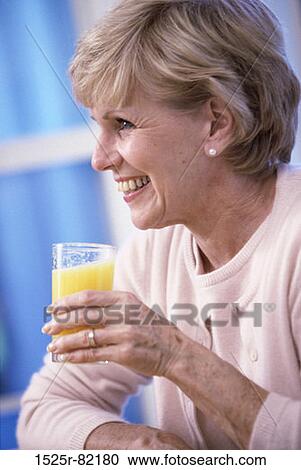 Stock Image - Elderly woman holding a glass of orange juice. Fotosearch