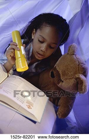 Stock Image - Girl reading a book under the sheets with a flashlight. Fotosearch