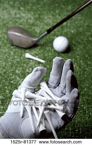 Stock Photo - Person's gloved hand holding tees with a golf club and a ball in the background. Fotosearch
