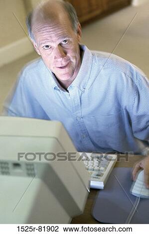 Stock Image - Portrait of a senior man sitting in front of a computer monitor. Fotosearch