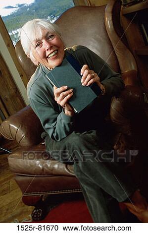 Portrait of a woman sitting on a couch holding a book View Large Photo Image Stock Image - Portrait of a woman sitting on a couch holding a book. Fotosearch