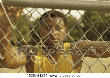 Portrait of a young man leaning against a chain-link fence View Large Photo Image Picture - Portrait of a young man leaning against a chain-link fence. Fotosearch
