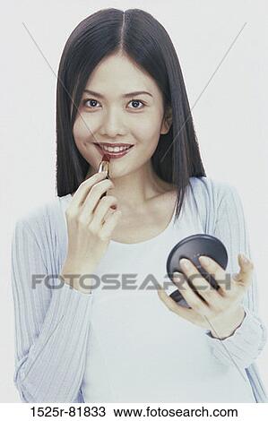 Portrait of a young woman applying lipstick View Large Photo Image Stock Image - Portrait of a young woman applying lipstick. Fotosearch