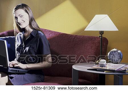 Portrait of a young woman sitting on a couch using a laptop View Large Photo Image Stock Photo - Portrait of a young woman sitting on a couch using a laptop. Fotosearch